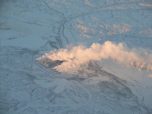 A plane flying over a snow covered area with smoke coming out of it.