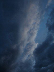 A cloudy sky with a plane flying in the sky.