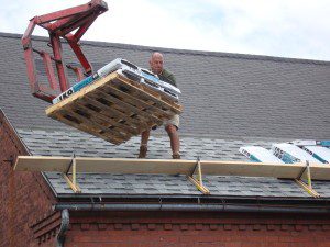 A man lifting a pallet onto a roof.