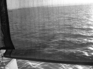 A black and white photo of a window with a view of the ocean.