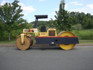 A yellow road roller is parked on the side of the road.