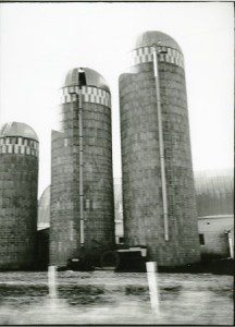 A black and white photo of three silos in a field.