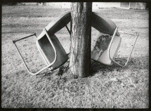 A black and white photo of a chair next to a tree.