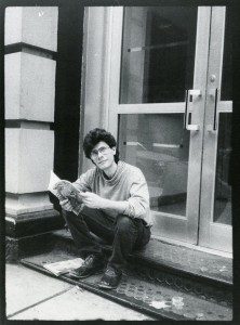 A man sitting on the steps of a building reading a newspaper.