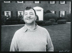 A man in a sweater standing in front of a house.