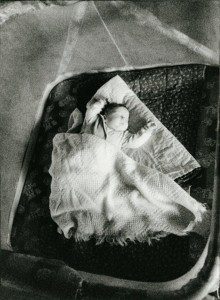 A black and white photo of a baby laying in a bed.