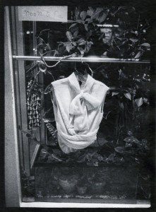 A black and white photograph of a dress hanging in a window.