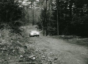 A car driving down a dirt road in the woods.