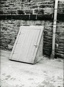An old black and white photo of a wooden door against a wall.