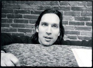 A black and white photo of a man leaning against a brick wall.
