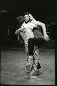 A black and white photo of two men hugging in a dance studio.