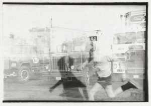 A black and white photo of a person running in front of a truck.