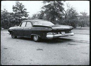 A black and white photo of an old car parked on the side of the road.