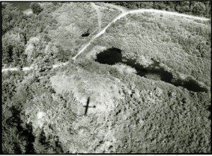 A black and white photo of a cross in the middle of a field.