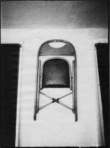 A black and white photo of a chair hanging on a wall.