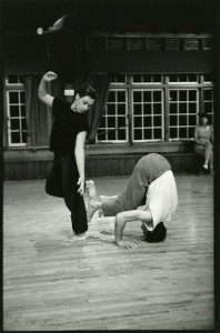 Black and white photo of a man doing a handstand on a wooden floor.