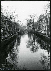 A black and white photo of a canal in amsterdam.