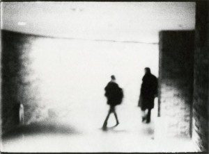 A black and white photo of two people walking down a hallway.