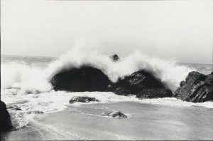 A black and white photo of a wave crashing into rocks.